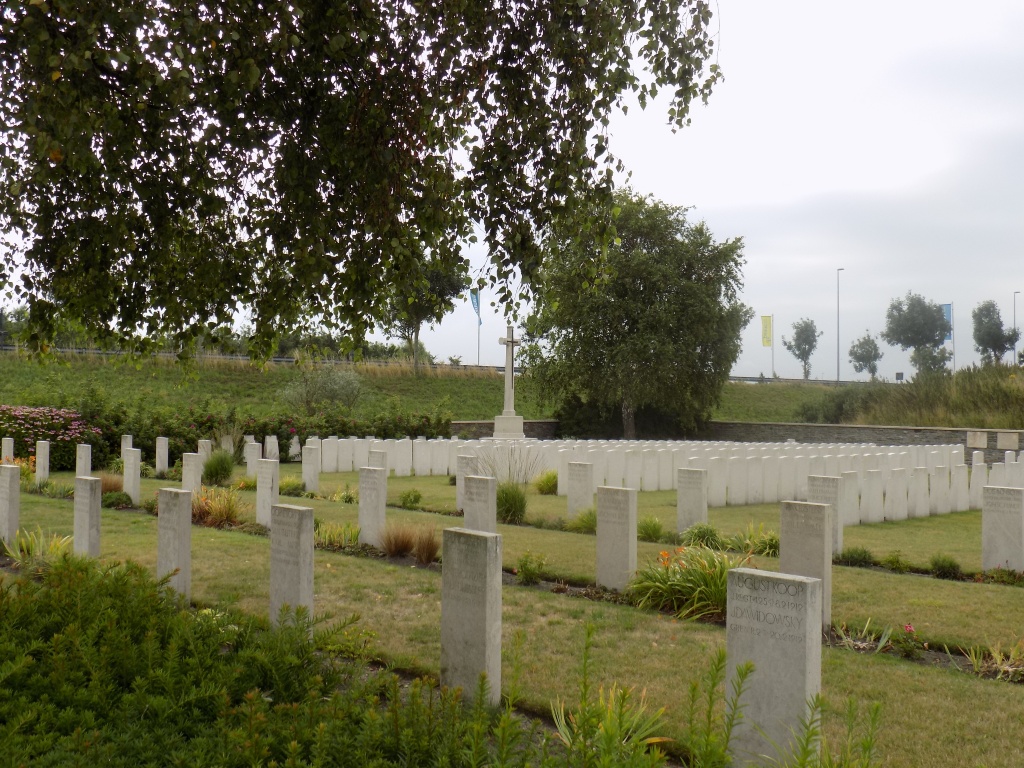 A colour photograph of rows of white graves with a hill in the background with trees on it.