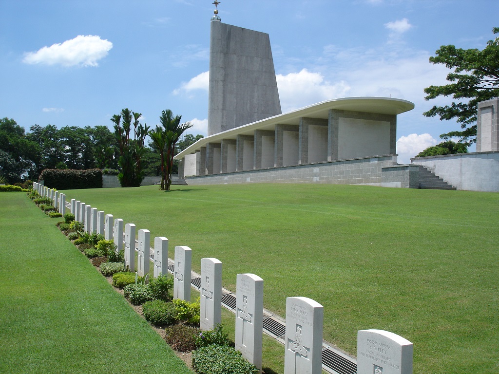 One line of white gravestones lead up the grass hill towards a large white memorial