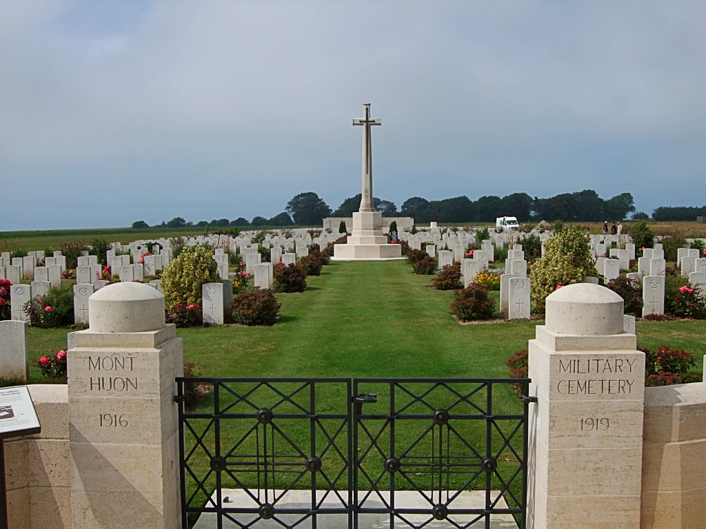 the entrance gates to the cemetery bear the inscription mont huon military cemetery 1916 1919. rows of gravestones lead up to the white cross of sacrifice