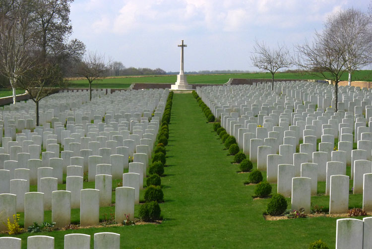 Many rows of white gravestones lead up towards a white stone cross in the background