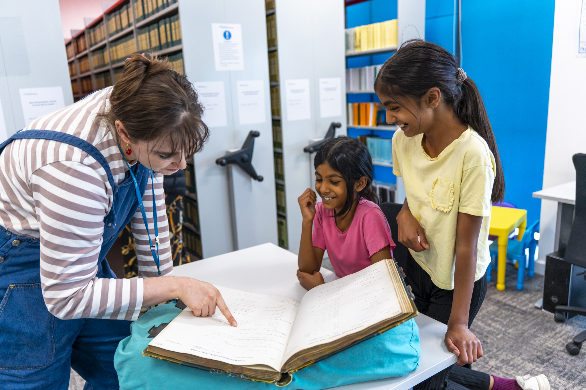 An archive staff member looking over archives with two girls